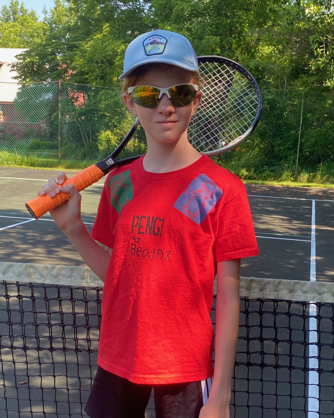 Kid at tennis court wearing red Pengi shirt with racket