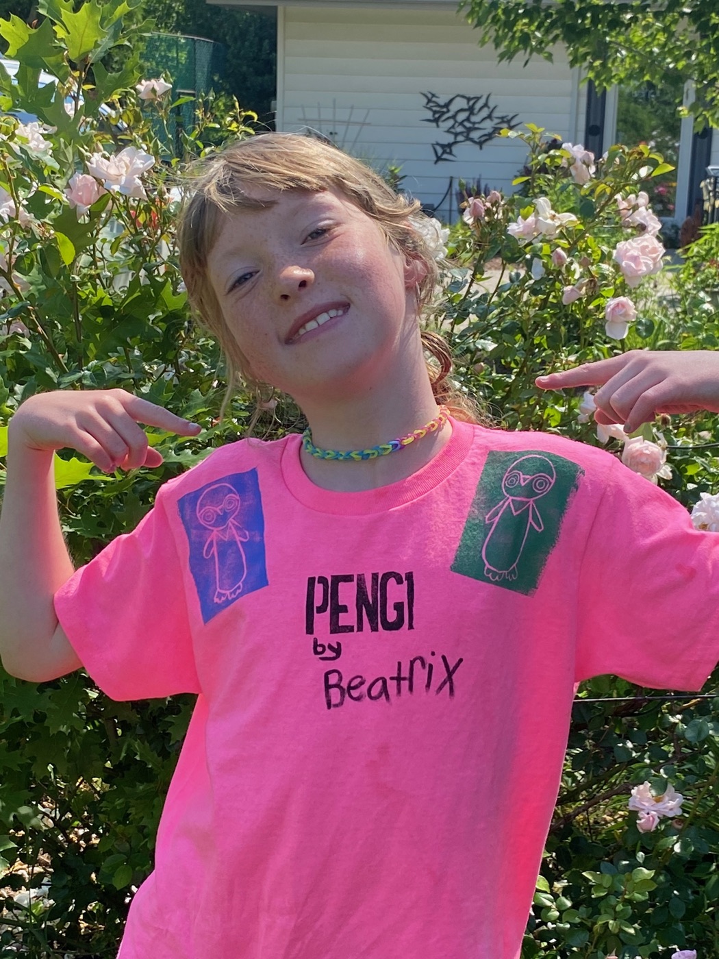 Beatrix proudly pointing at her Pengi shirt in the garden
